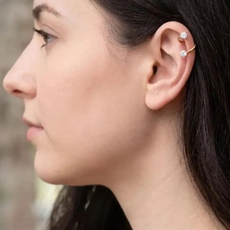 A close-up side profile of a woman wearing a gold ear cuff with two small clear gemstones on the helix.
