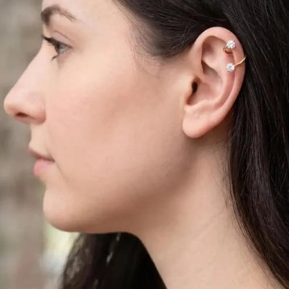 A close-up side profile of a woman wearing a gold ear cuff with two small clear gemstones on the helix.