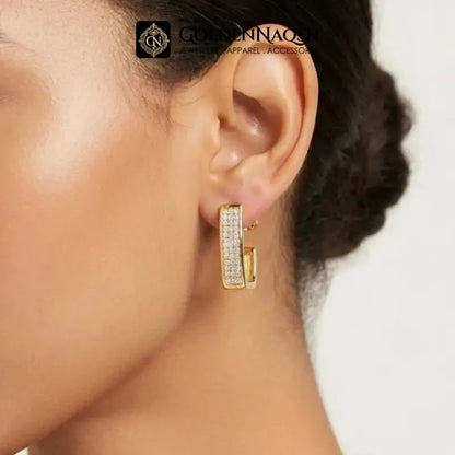A close-up of a model's ear wearing a gold hoop earring adorned with small clear pavé stones. The brand logo 'Goldennacci' is visible at the top of the image.