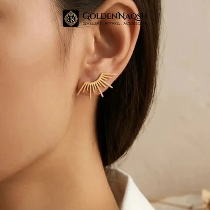A close-up of a model's ear wearing a delicate gold crescent sunburst stud earring. The image features a watermark for 'GOLDENNAOQi JEWELLERY APPAREL ACCENTS' at the top.