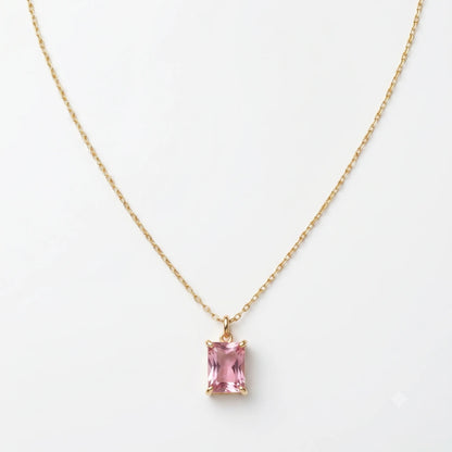 Gold necklace with a pink gemstone pendant on a white background