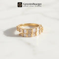 A gold ring with baguette-cut clear stones, displayed on a white marble surface with a soft shadow. The brand logo 'GOLDENNAQSH' is visible at the top of the image.