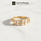 A gold ring with baguette-cut clear stones, displayed on a white marble surface with a soft shadow. The brand logo 'GOLDENNAQSH' is visible at the top of the image.