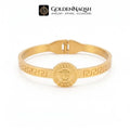 A gold-plated metal bangle bracelet featuring a central circular medallion with an embossed face motif and Greek key patterns along the band, displayed on a clean white background with the GoldenNaqsh brand logo at the top.