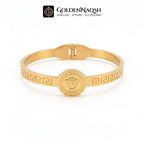 A gold-plated metal bangle bracelet featuring a central circular medallion with an embossed face motif and Greek key patterns along the band, displayed on a clean white background with the GoldenNaqsh brand logo at the top.