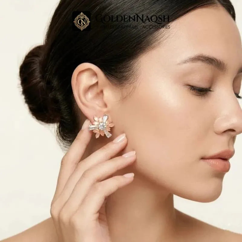 A close-up lifestyle shot of a woman wearing a gold flower-shaped stud earring with clear crystals, touching her ear with her hand. The brand logo 'GOLDENNAOSH' is visible at the top.