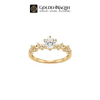 A yellow gold ring with a round-cut clear center stone and smaller accent stones along the shoulders, shown on a plain white background with the GoldenNaqsh brand logo at the top.