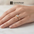 A gold ring with a clear central gemstone and decorative side details, shown worn on a hand. The GoldenNaqsh brand logo is visible at the top of the image.