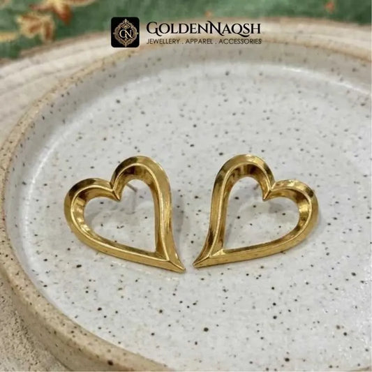 A pair of gold heart-shaped stud earrings displayed on a speckled ceramic plate, with the brand logo 'GOLDENNAQSH' at the top.