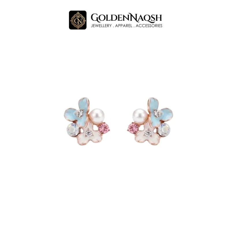 A pair of flower-shaped stud earrings by GoldenNaqsh, featuring iridescent light blue and pink enamel petals, a white faux pearl, and a small pink crystal, set in rose gold on a white background.