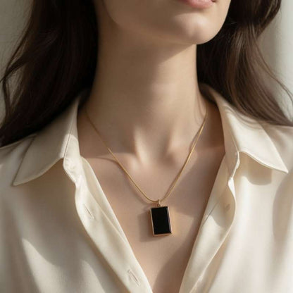 Necklace with a black pendant worn by a person in a white shirt
