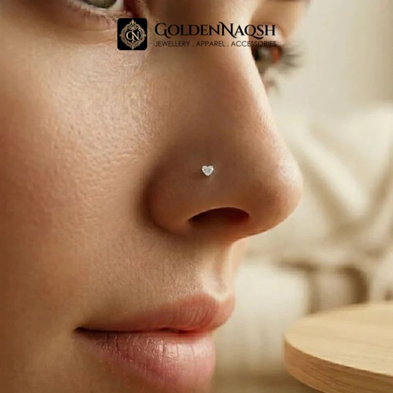 Close-up of a woman's nose wearing a small heart-shaped silver stud nose ring, with the GoldenNaosh brand logo at the top.