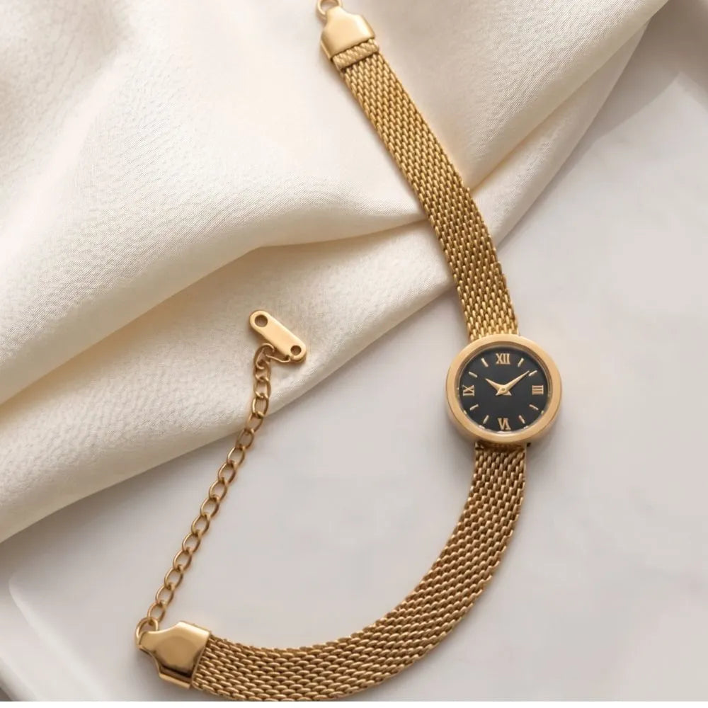 Golden Naqsh Watch Bracelet featuring a gold mesh chain strap and a black mini watch face with Roman numerals resting on white silk