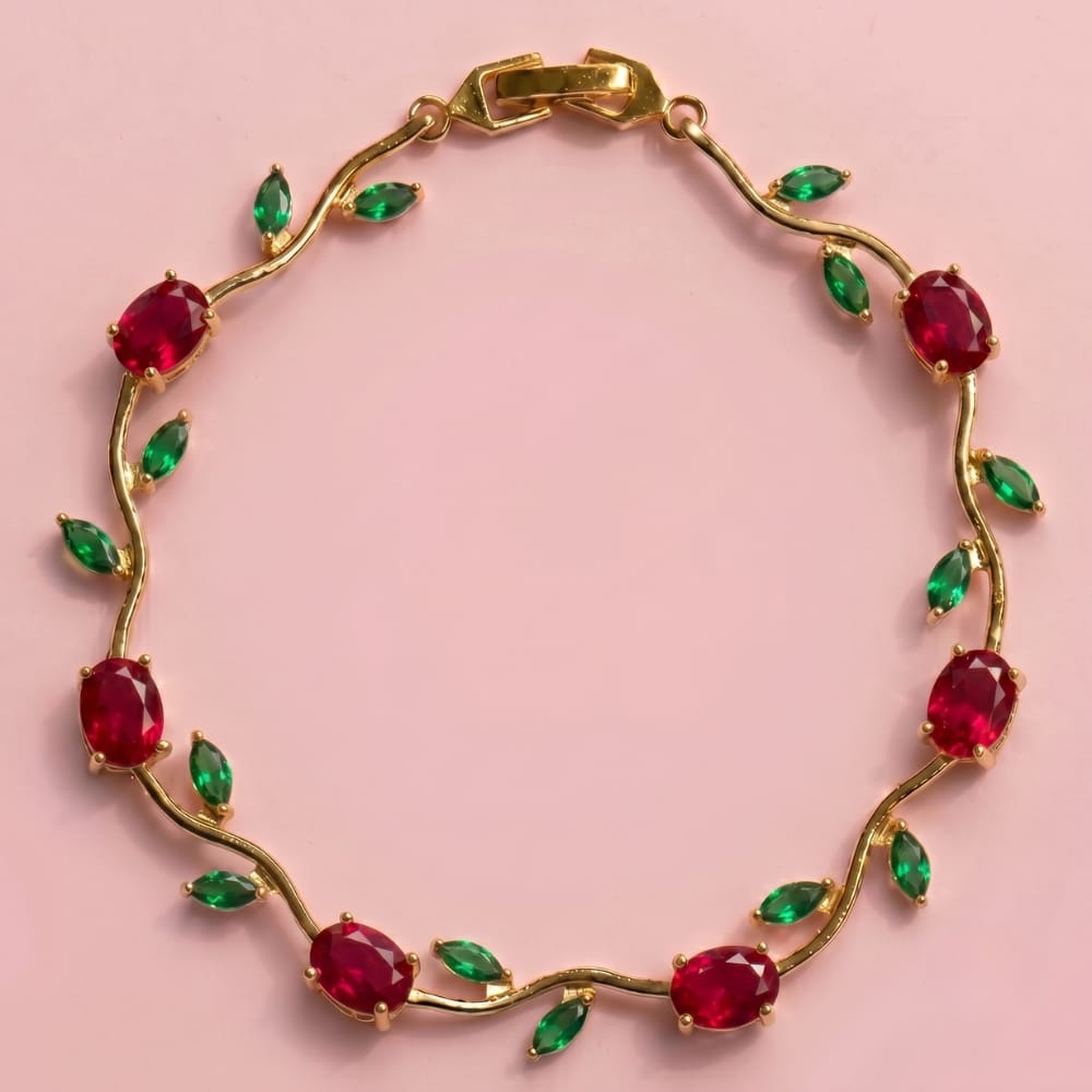 Gold bracelet with red and green gemstones on a pink background