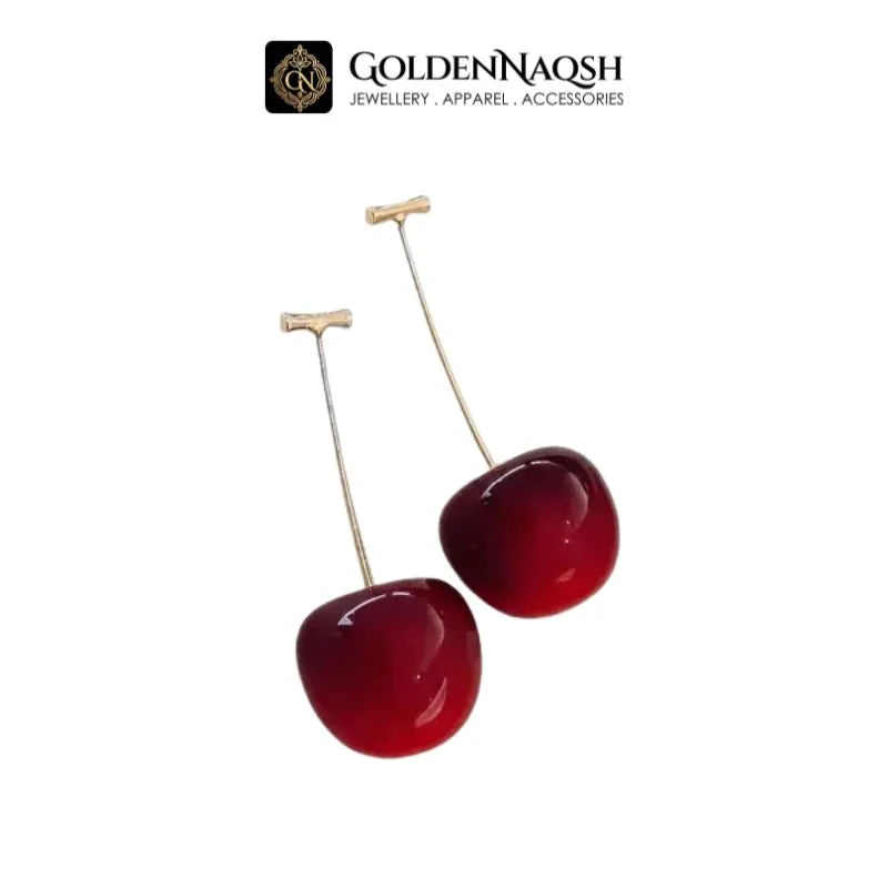 A pair of dangling cherry earrings with glossy deep red cherry-shaped drops and thin gold-toned stems, shown on a plain white background with the GoldenNaqsh brand logo above.