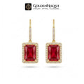 A pair of Goldenaqsh rectangular drop earrings in yellow gold, featuring a large red faceted gemstone in the center, surrounded by a halo of small clear stones, with gold hooks and pavé-set side details, shown on a white background with the brand logo at the top.
